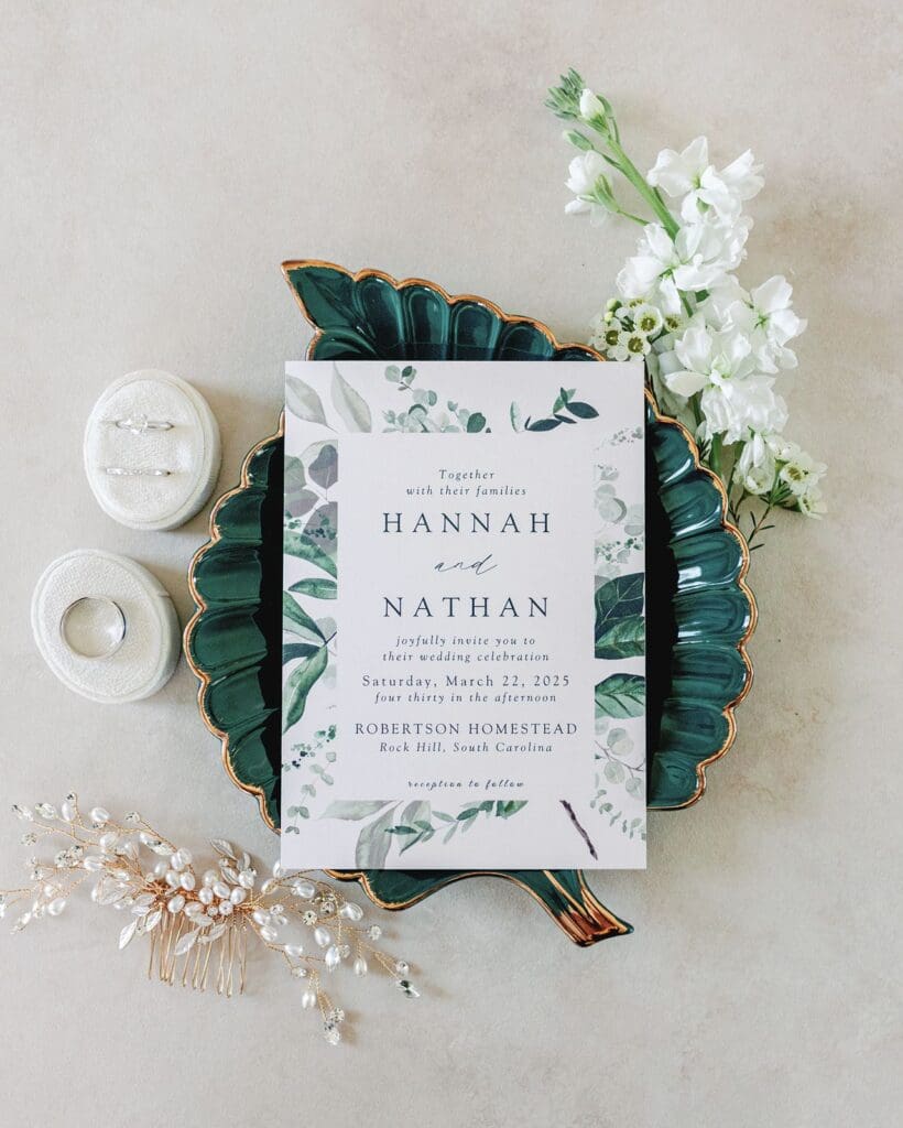 Flat lay wedding details including an invitation, rings and a bridal hair piece